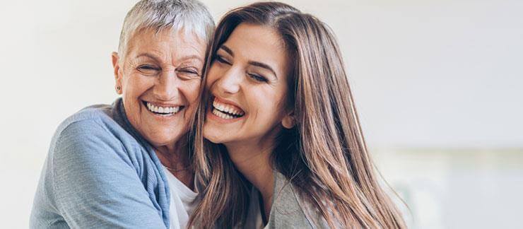 Senior woman smiles while embracing adult daughter.