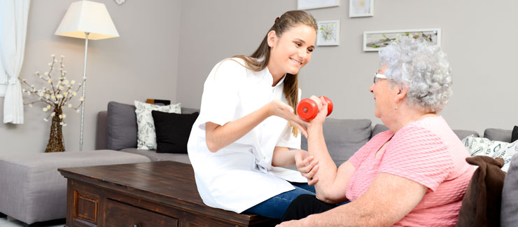 Female care worker helps elderly woman exercise with hand weights.