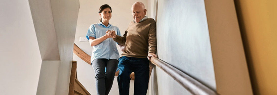 Female caregiver helps elderly man down the stairs as part of fall prevention program.