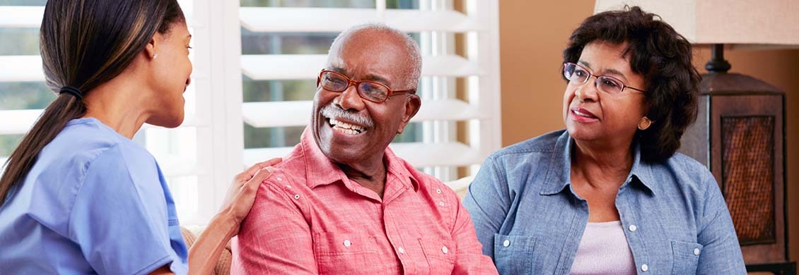 Elderly couple is happily speaking to a home caregiver during a visit.