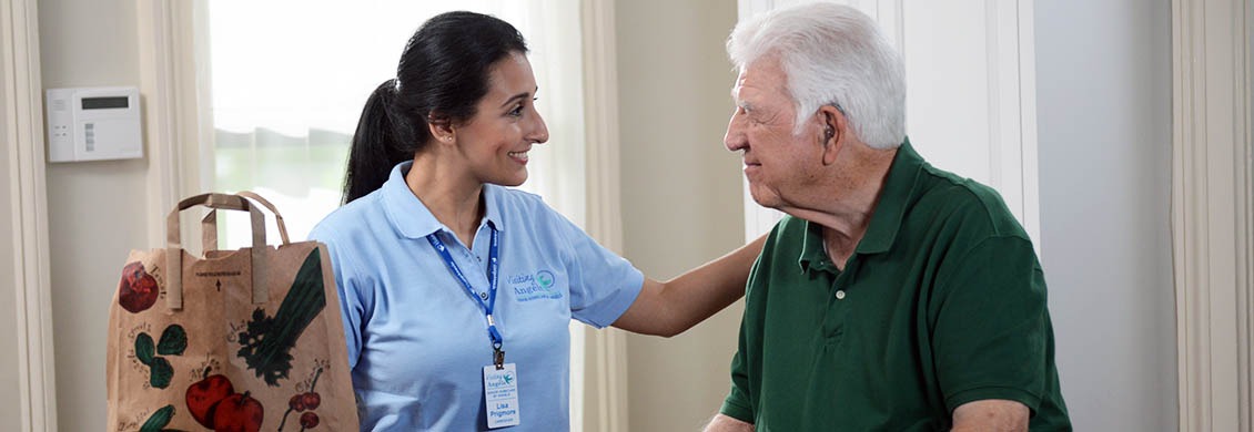 In-home personal care provider bringing bag of groceries to elderly man at home.