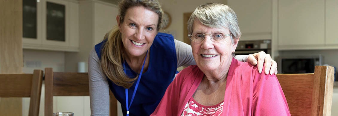 Home care worker shares a smile with elderly woman at the kitchen table.