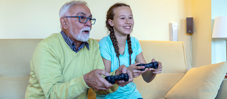 Teenage granddaughter provides senior care by playing video game with senior grandfather at home.