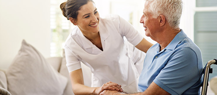 Home care nurse helps a senior man in a wheelchair at home.