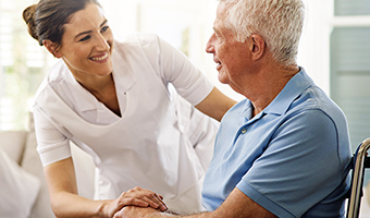 Home care nurse helps a senior man in a wheelchair at home.