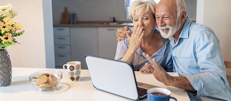 Senior couple in kitchen enjoying a long-distance video chat session with their family.