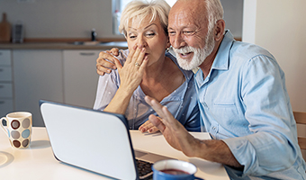 Senior couple in kitchen enjoying a long-distance video chat session with their family.