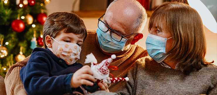 Elderly couple with masks sit with grandson holding a toy he received at Christmas.